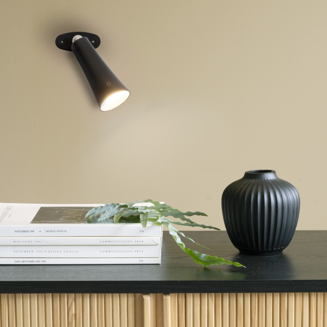 Modern svart bordslampa med vridbar armatur, LED-belysning och uppladdningsbart batteri, placerad på skrivbord.