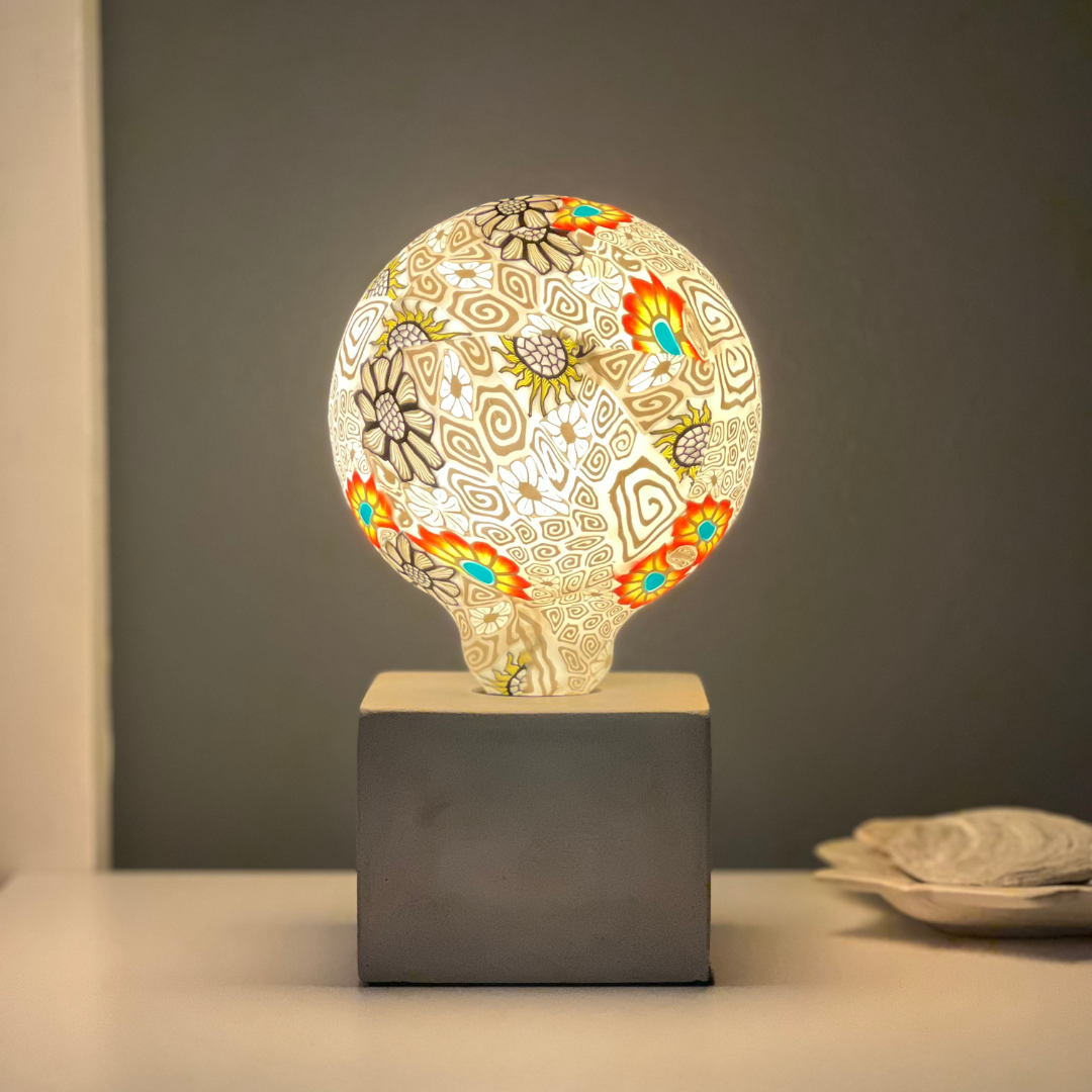 Blomman LED-glödlampa med färgglad blomdekor i lampfot på sidobord. Dekorativ Blomman LED-lampa tänd i modern miljö, unik blomdesign.