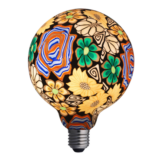 Blomman Flerfärgad LED-glödlampa med livlig blomdekor och varmvit sken. Närbild på Blomman Flerfärgad med flerfärgade blommor på glaset. Blomman Flerfärgad LED-lampa i lampfot på sidobord – dekorativ inredningsdetalj.