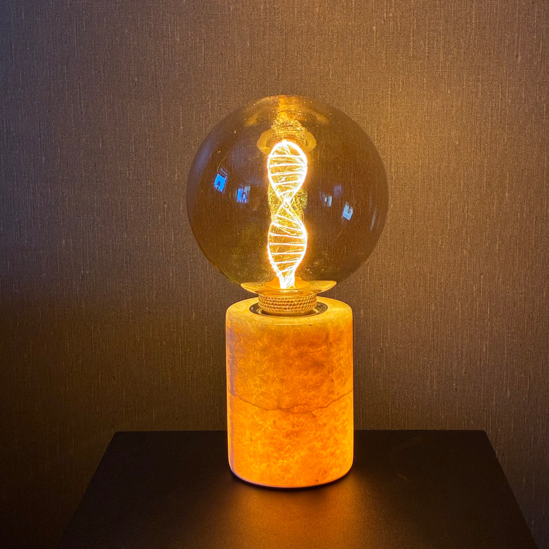 mörk marmor bordslampa med dna glob i guld och varmt ljus. klar beige marmorfot till bordslampa som lyser upp inifrån. Snygg marmorlampa i hemmamiljö. 