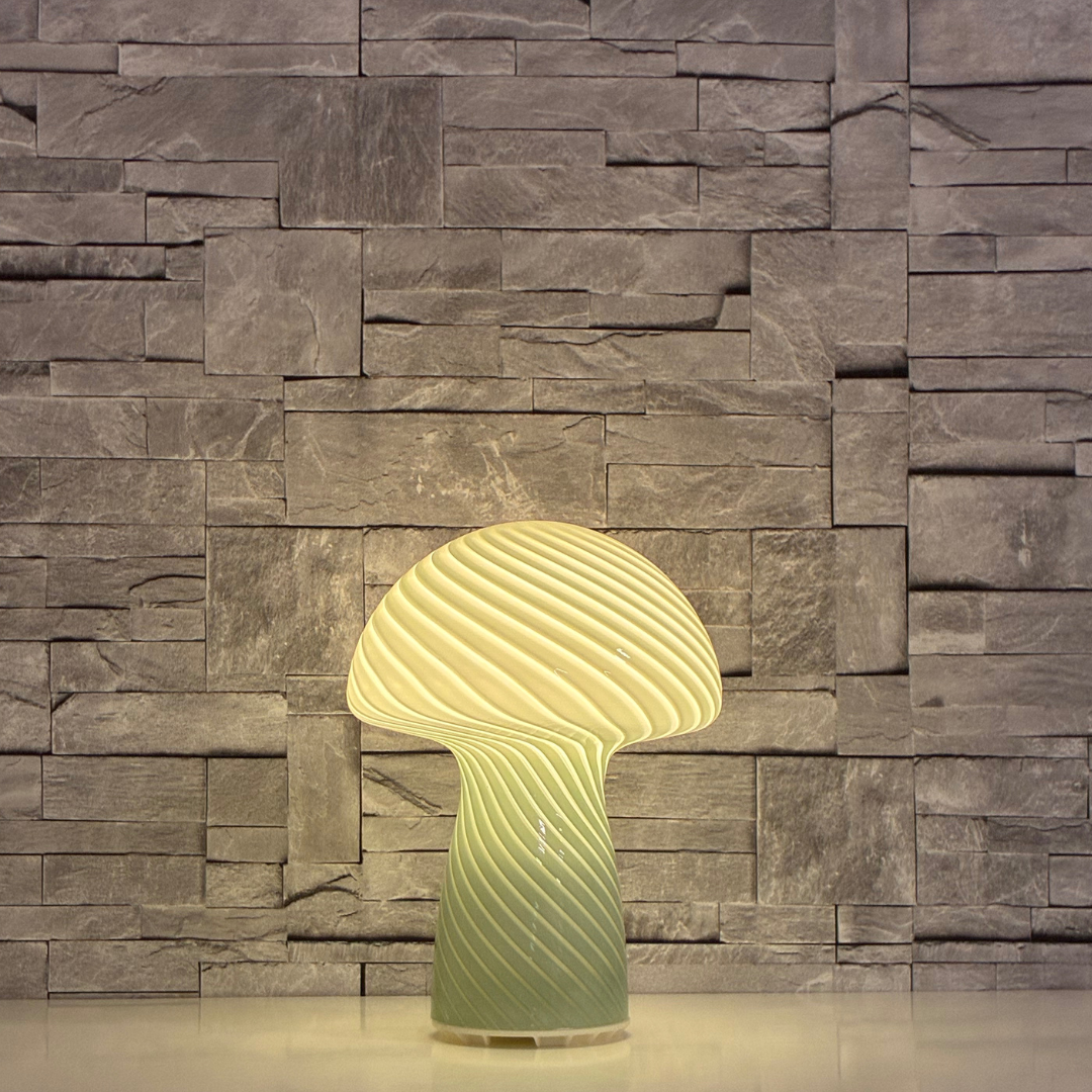 Svamplampa Glas Grön med varmvitt sken mot stenbakgrund. Grön svamplampa i glas. Grön vardagsrumslampa på soffbordet. Grön glaslampa i svampform med sneda ränder och LED-belysning.